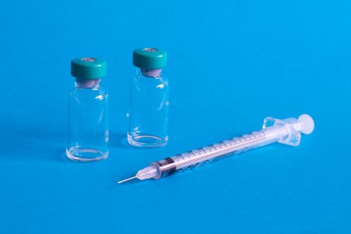 A closeup of a syringe needle with the vaccine ampoules against a blue background - COVID-19
