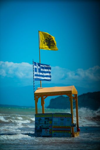 A vertical shot of the greek flag on a post at the beach