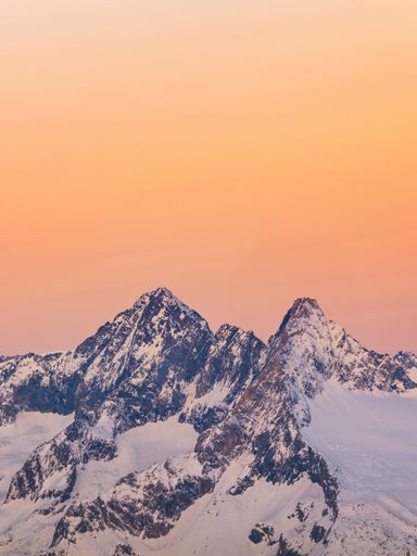 A vertical shot of rocky mountains covered in the snow during a beautiful sunset in Sondrio, Italy