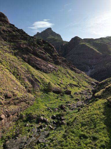 An aerial view of a rocky hill, with a stream flowing through it and a majestic mountain range in the background