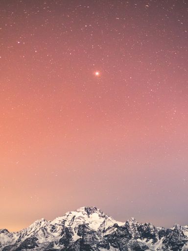 A vertical shot of rocky snowy mountains under a starry sky in the evening in Sondrio, Italy