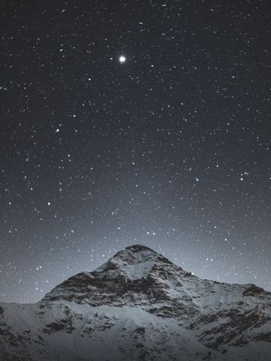 A vertical shot of rocky snowy hills under a beautiful starry sky at night in Sondrio, Italy