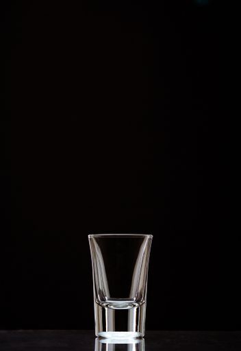A vertical shot of an empty shot glass isolated on a black background