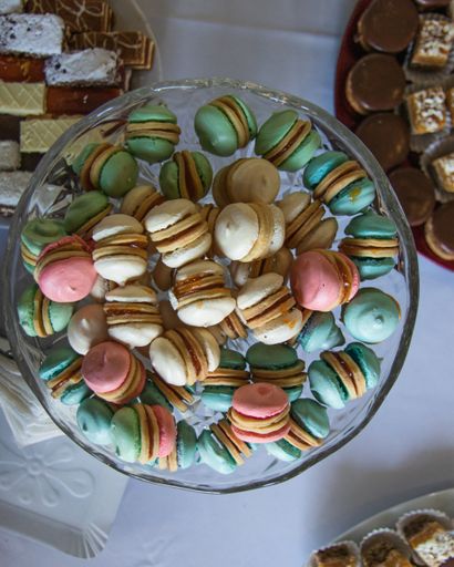 A close up shot of colorful macarons in a glass bowl with some desserts on the side