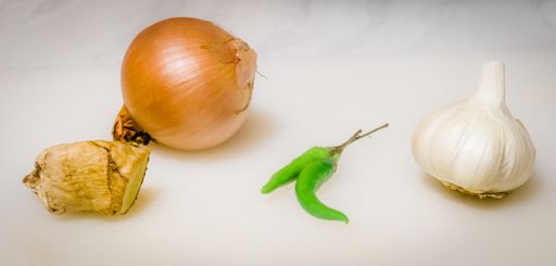 An onion, garlic, green chili peppers, and ginger on a white surface