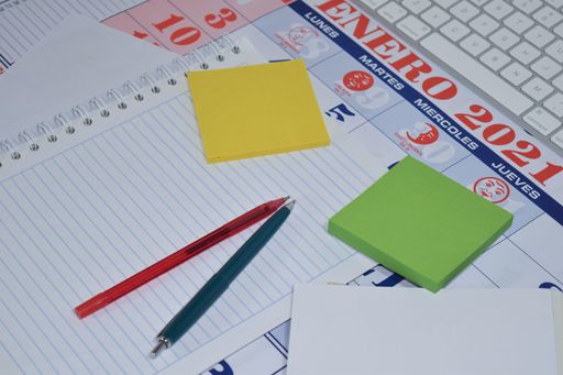 A selective focus shot of notepad, pens, papers, and sticky notes on a calendar in Spanish