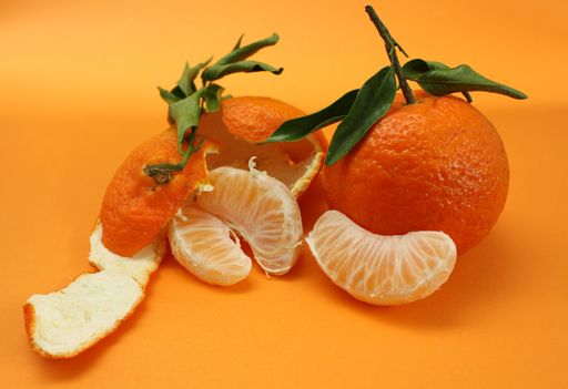A closeup shot of a whole tangerine and some slices on an orange