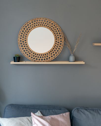 A vertical shot of room decor with a round woven frame with a white center and reed in a vase hanging on a wall