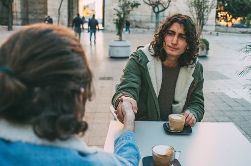 Picture of Informal Handshake Between Two Young Male Friends With Long Hair Having a Big Cup of Coffee in a Table Bar Terrace at Street