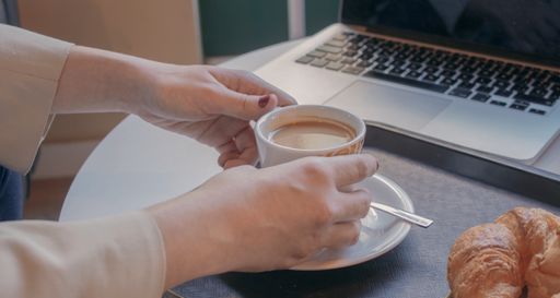 A selective focus shot of a female's hands taking the cup of coffee from the table
