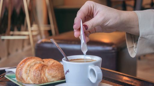 A selective focus shot of a female's hand pouring sugar in the coffee
