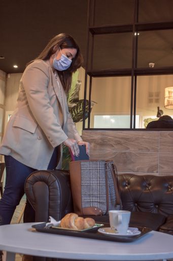 A vertical shot of a young lady taking her laptop from her bag wearing a sanitary mask at a cafe