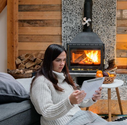 A female watching a movie on her tablet in a wooden house next to the fireplace stove