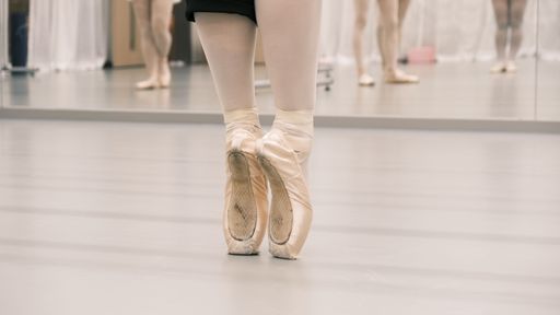 A close-up shot of a the feet of a ballet dancer doing a releve on pointeshoes