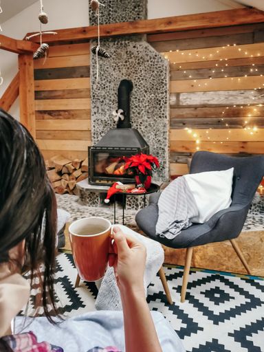 A female drinking coffee and relaxing on the couch in a room decorated with Christmas decorations
