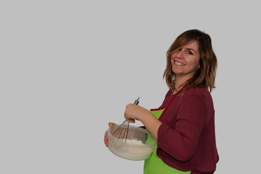 A Caucasian female wearing a green apron, cooking with a whisker on a white background