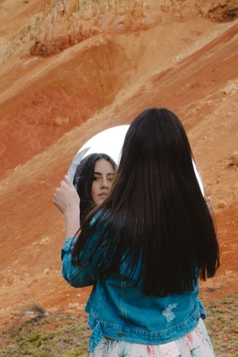 A vertical shot of a young beautiful female posing with a mirror in the Sabrinsky desert of Colombia
