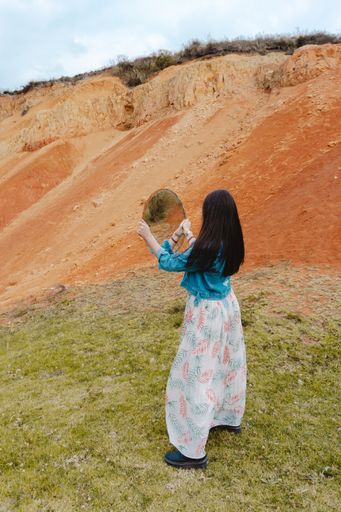 A vertical shot of a young beautiful female posing with a mirror in the Sabrinsky desert of Colombia
