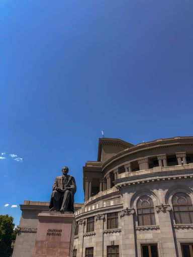 A vertical shot of Hovhannes Tumanyan statue on the background of Opera in daylight