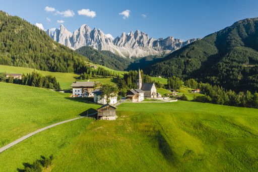 A high angle shot of a lot of buildings surrounded by high rocky mountains in Funes Valley, St. Italy