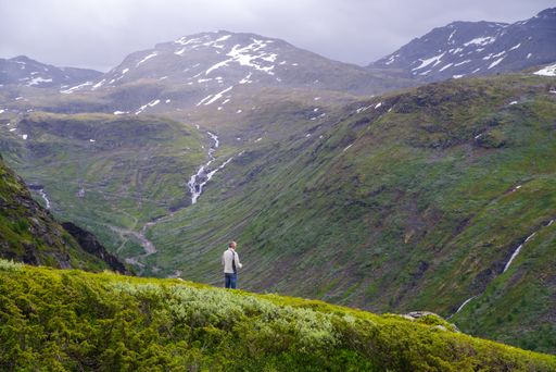 A man stands at the edge of a precipice on a mountain peak, enjoying the breathtaking view.