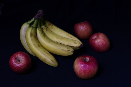A high angle shot of delicious bananas and apples on a black surface
