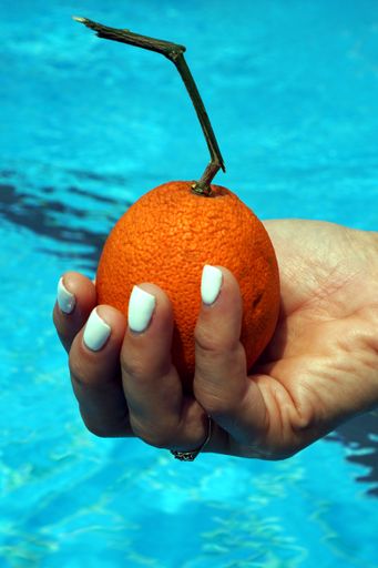 A vertical closeup shot of a female hand holding a wrinkled orange a swimming pool