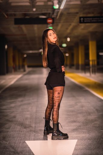 A shallow focus of a young female wearing a black jacket with shorts and boots and posing in an underground car park