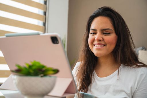 A selective focus shot of a cheerful Hispanic lady doing a video call from home using a tablet