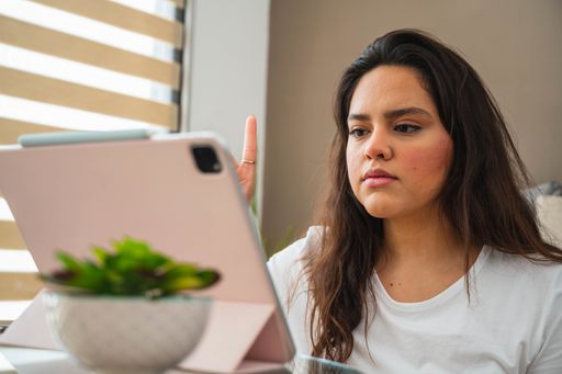 A selective focus shot of a young Hispanic lady doing a video call from home using a tablet