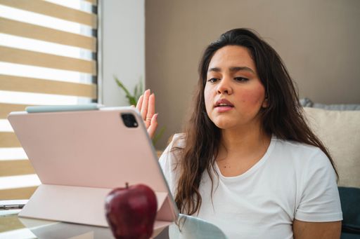 A selective  focus shot of a young Hispanic lady during a video call from home with her tablet