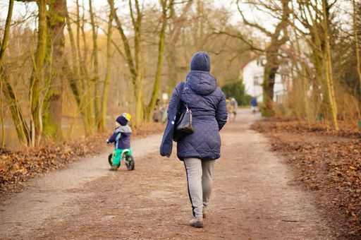 Adult woman walking on a footpath in the Debiec forest on a cold winter day. Child on bike in soft focus background.