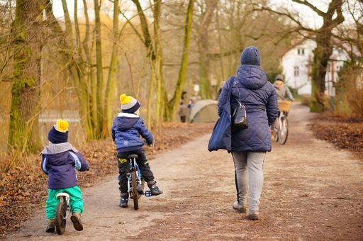 Woman and two small kids on bicycles on a footpath in the Debiec park on a cold winter day.