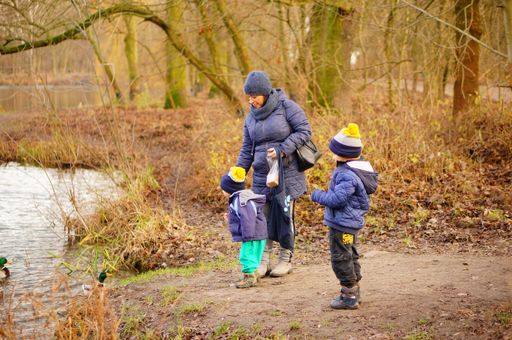 Woman and two kids standing by a pond feeding ducks in the Debiec forest.