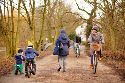 Walking woman next to kids and adult on bicycles on a footpath in the Debiec forest on a cold winter day.