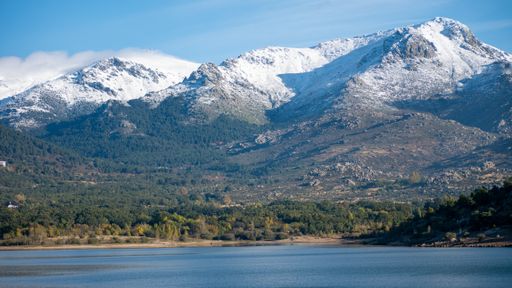 A lake surrounded by hills covered in greenery and the snow under a blue sky and sunlight