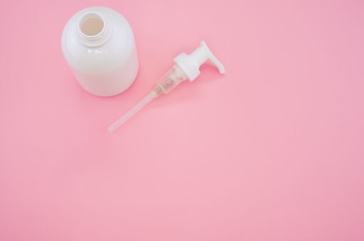 A high angle shot of a white bottle and a pump lid on a pink background
