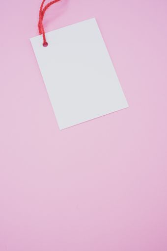 A vertical shot of a blank tag with a red string on a pink background