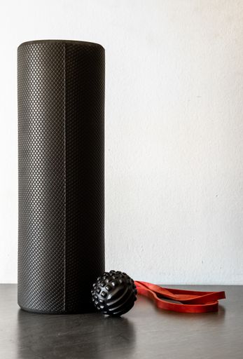 A black foam roller, massage ball, and resistance band for fitness, recovery, yoga, and pilates
