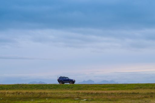 A single car driving in a green grassy field under a cloudy sky in Icela