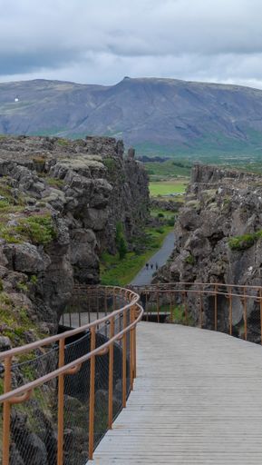 A vertical shot of a wooden walkway surrounded by rocky hills under a cloudy sky in a park in Iceland