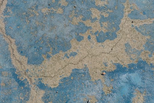 A closeup of an old grungy cement wall with weathered blue paint on it