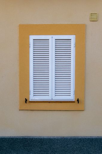 A vertical shot of an old window on a yellow exterior wall