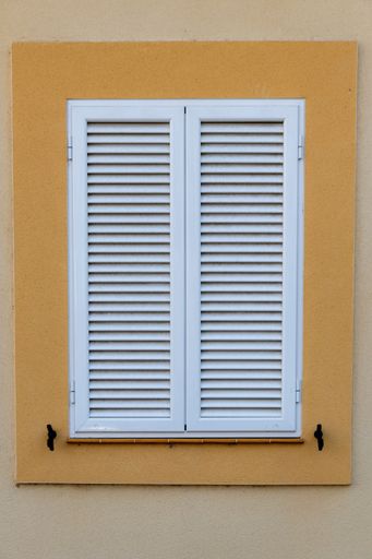 A vertical shot of an old window on a yellow exterior wall