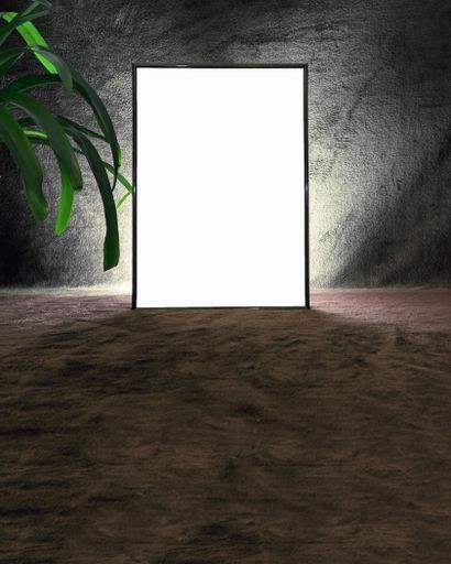 A vertical shot of a blank picture frame on a sandy ground with a cement wall in the background