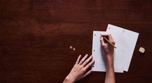 A top view of a person writing on a blank paper with a pencil on a wooden surface - copy space