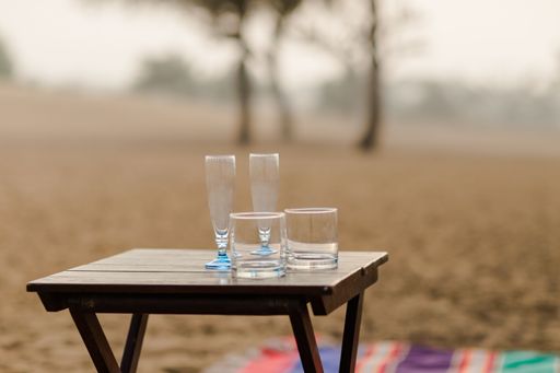 A closeup shot of four glass cups on a small wooden table on a colorful blanket in the field