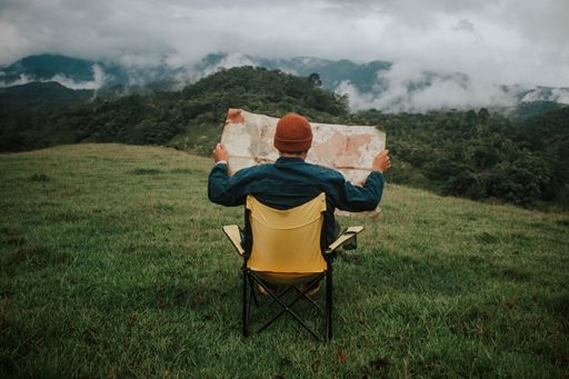 A man sitting on a foldable chair and looking at the map in an outdoor setting.