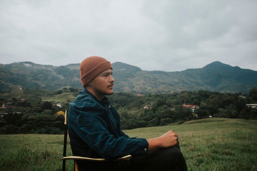 A man sitting on a foldable chair in a grassy valley surrounded by green hills.