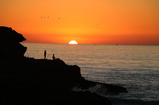 A man with a spinning rod fishing in the evening from the cliffs in the Atlantic ocean